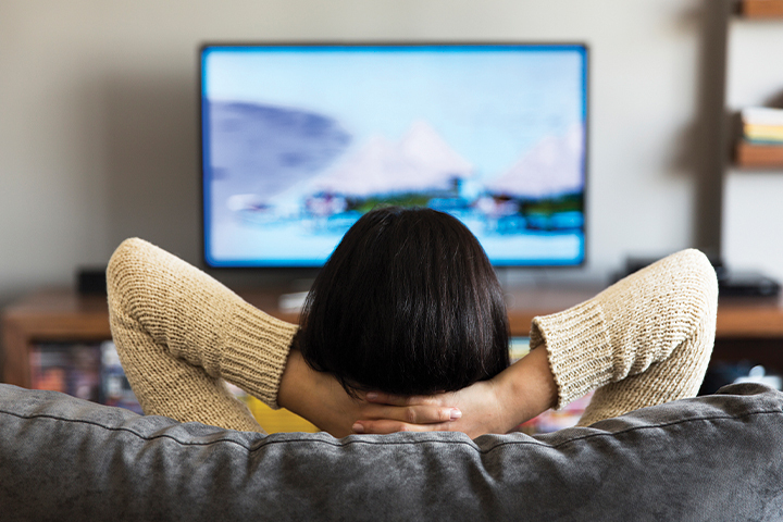 woman watching TV with arms behind head